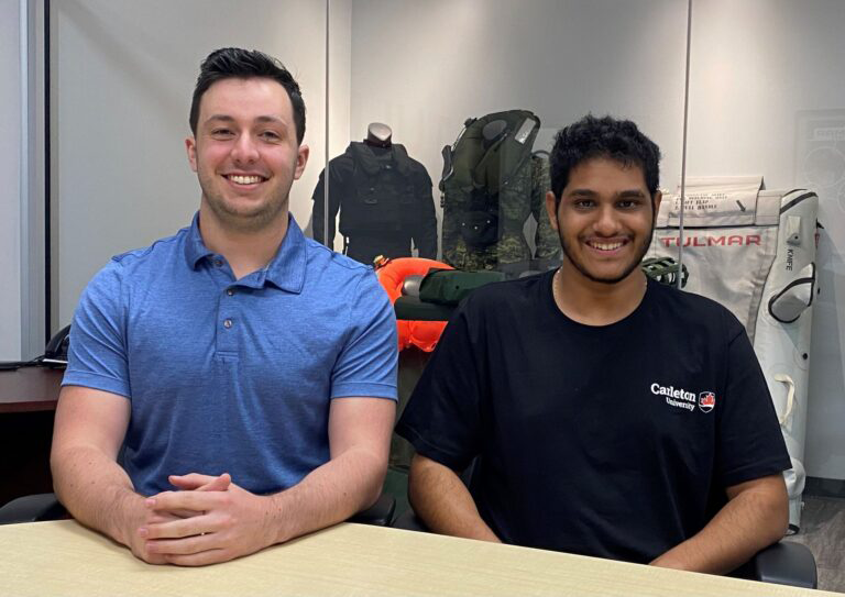 Two people sitting at a table with tactical gear displayed in the background.