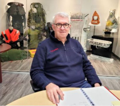 Patrick Tallon, président de Tulmar, en veste bleue, assis à une table avec un cahier ouvert, dans une salle où sont exposés des équipements de sécurité.