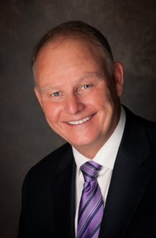 Man in suit with striped purple tie on a dark background.