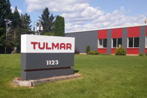 Sign reading "TULMAR" in front of a building with green lawn under a clear sky.