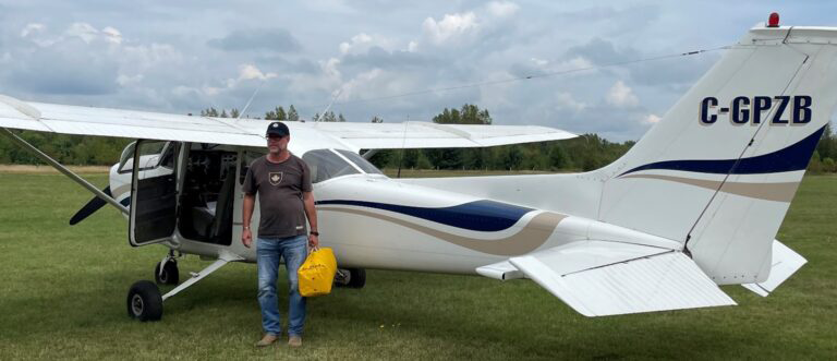 Une personne se tenant à côté d'un petit avion blanc à la porte ouverte, sur un terrain herbeux.