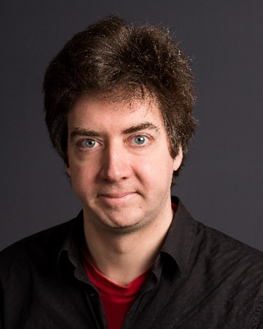 Man with dark hair wearing a black shirt and a red collar.