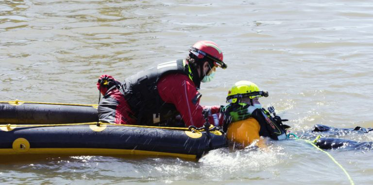 Two individuals in water rescue gear operating on an inflatable boat.