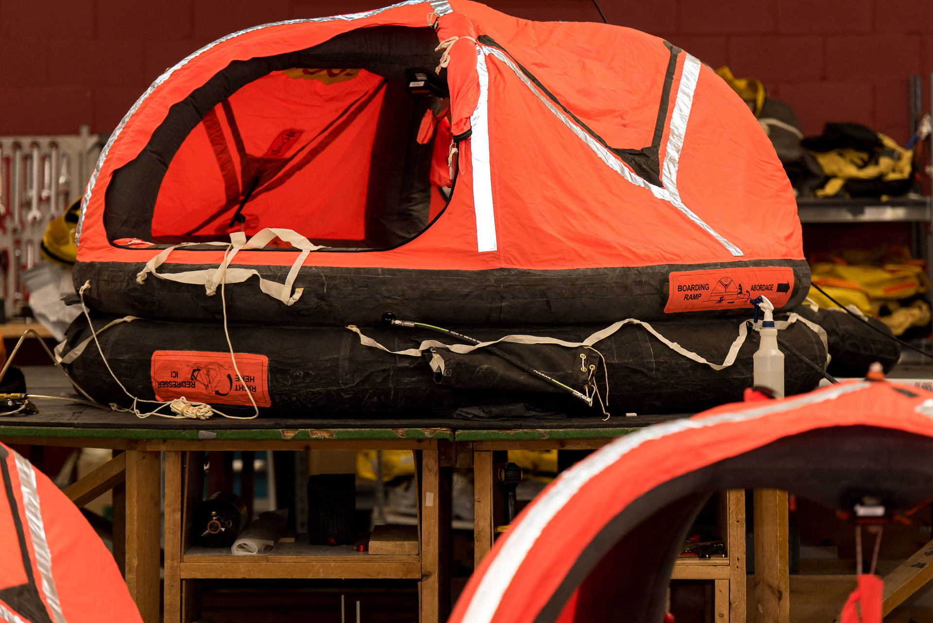 An inflated orange and black life raft on a wooden table in a workshop.