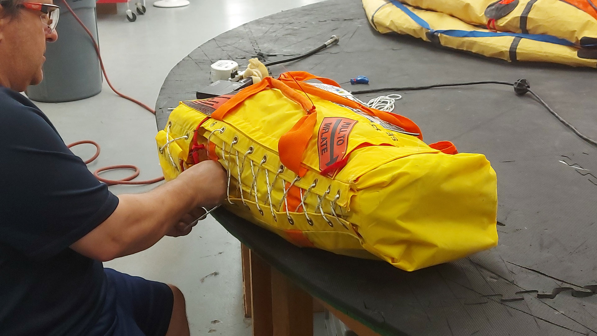 Person securing a yellow raft in a bag with lacing cords on a workbench.