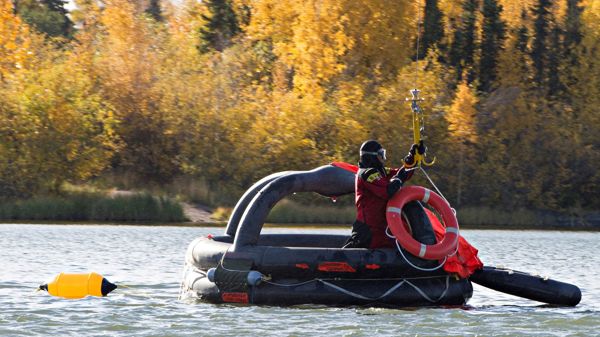 Person in a black and red outfit on an inflatable life raft a polly being lowered down to the person on the raft.