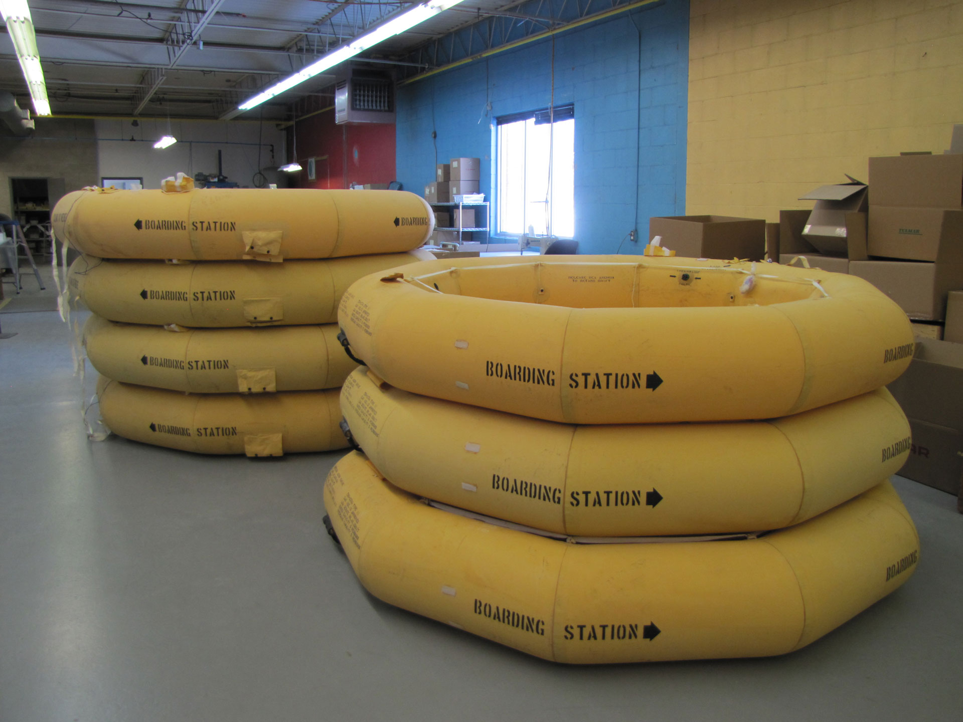 Stacked yellow inflatable rafts with "BOARDING STATION" text, inside an industrial room.