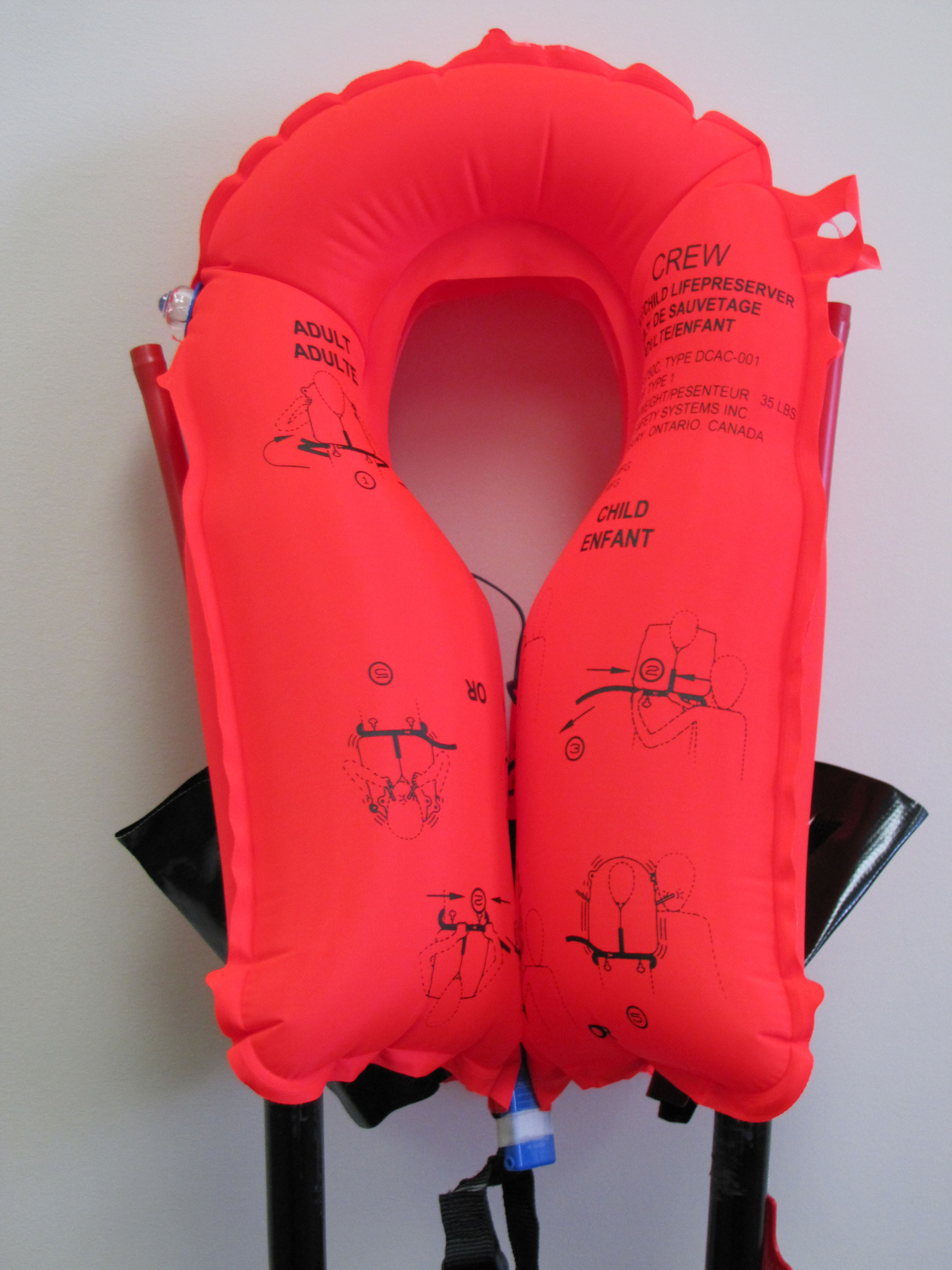 Bright red adult life jacket with instructional images, hanging against a white wall.