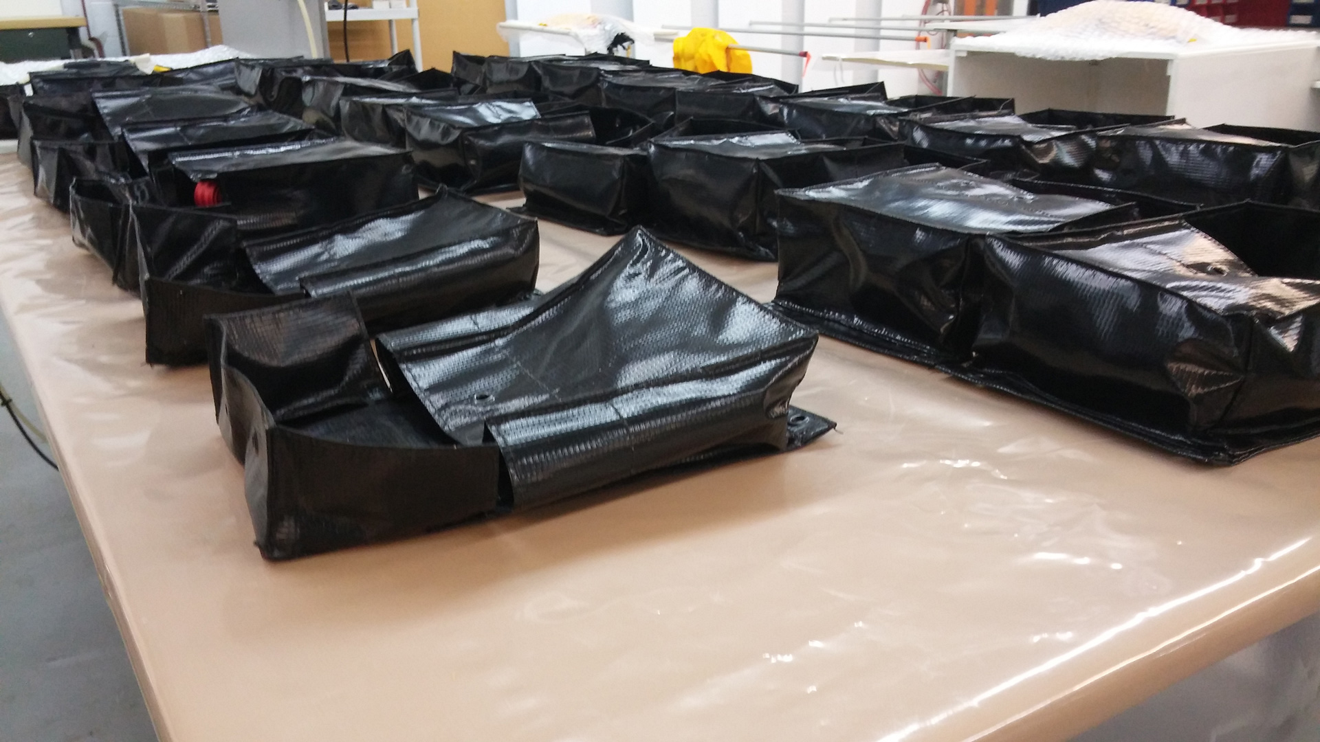 Black foldable bags for Passenger Restraint Kit arranged on a table in a workshop.