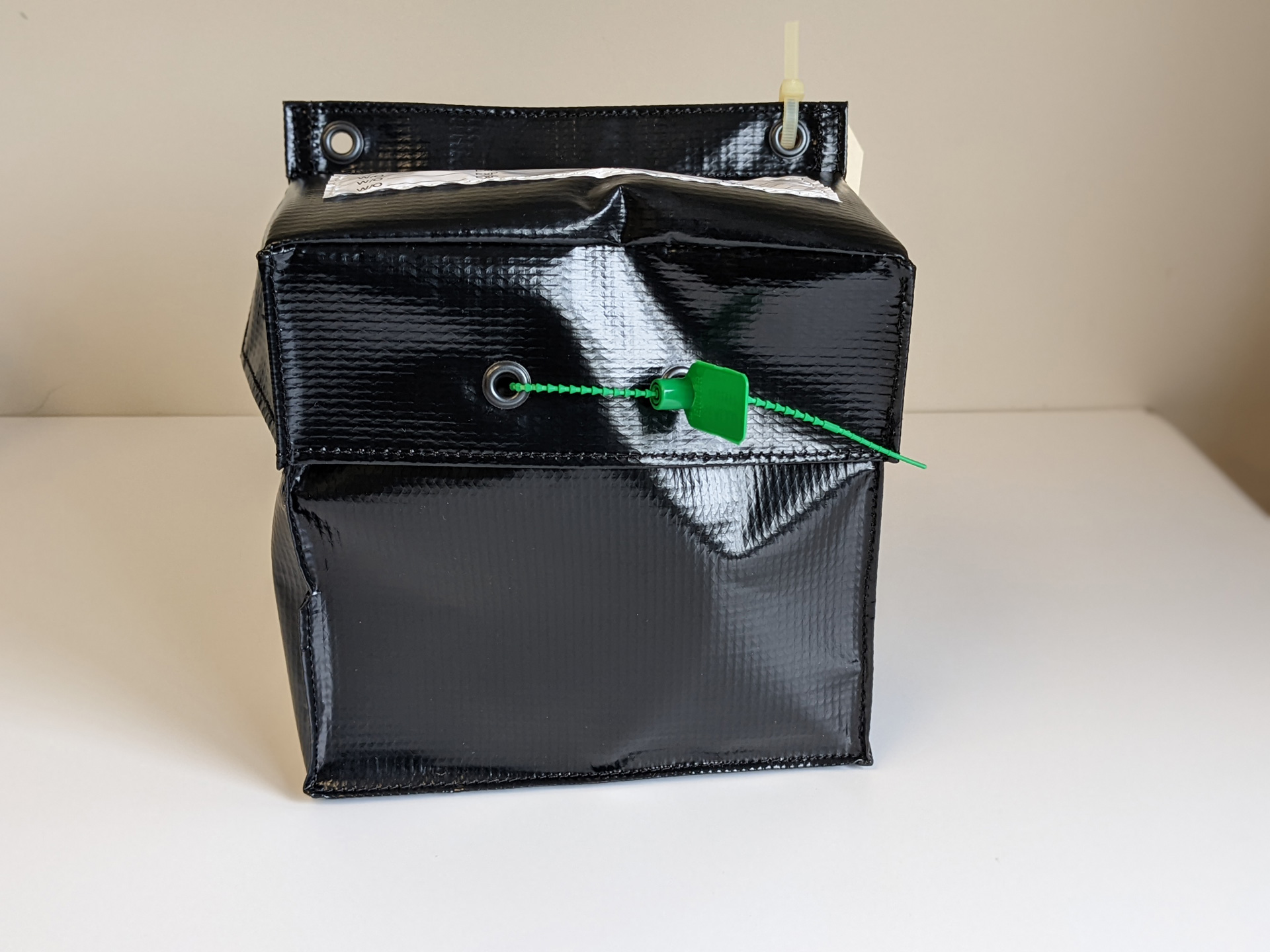 A black bag with a green tag indicating the tamper-free status of a Passenger Restraint Kit, closed and standing upright.