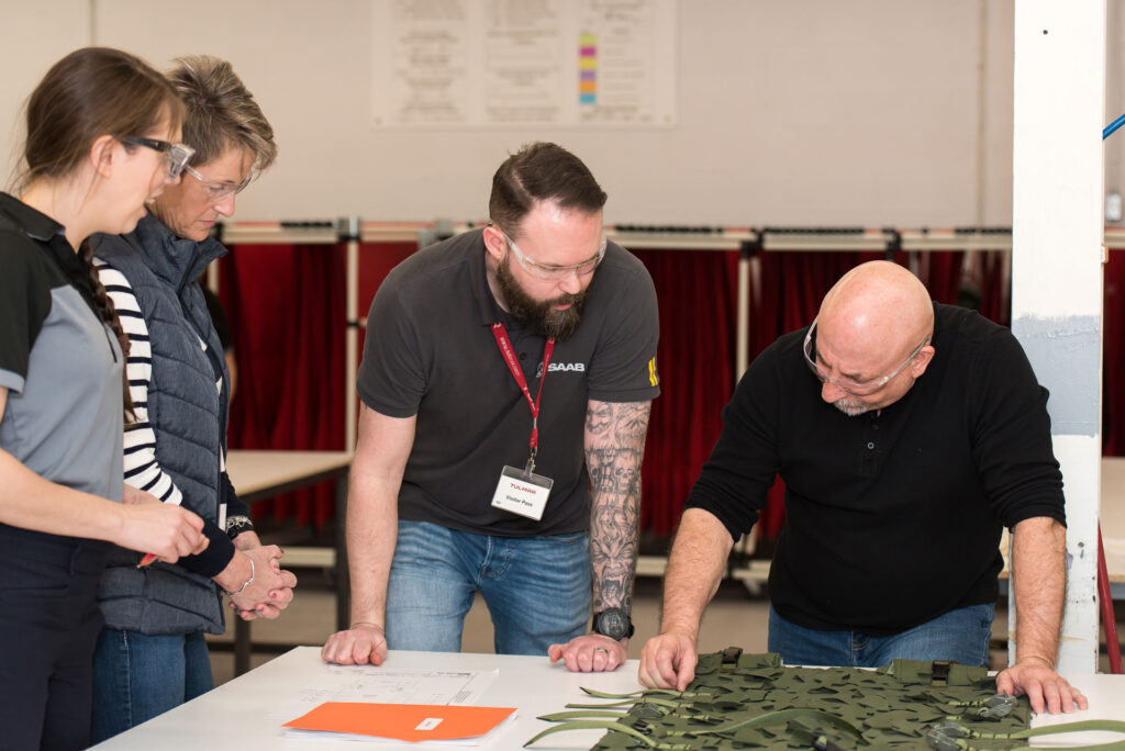 Four individuals standing around a table with documents and camouflaged gear.